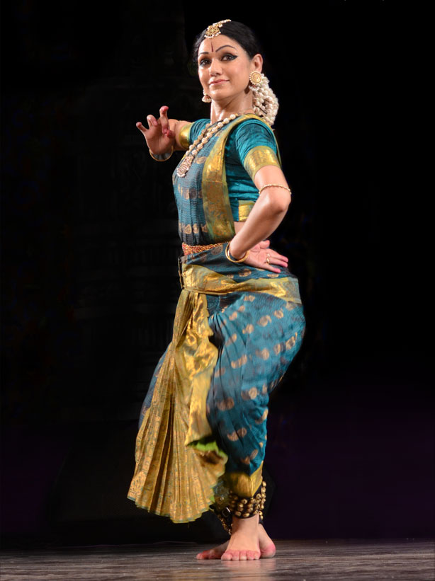 Rama in a teal and gold costume, one hand held near her shoulder